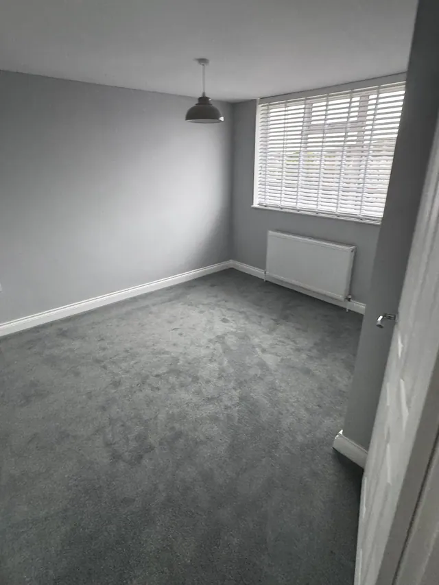 Finished bedroom with grey carpet and a window blind