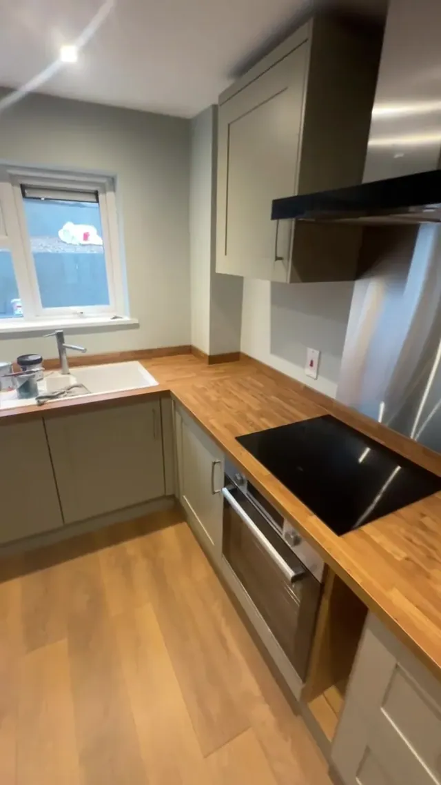 Fitted kitchen with hob, oven, extractor and wood-tone worktop at the finishing stage