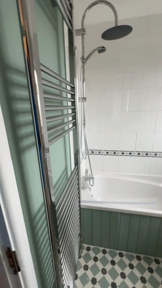 Refitted bathroom with green wall panelling, bath and shower screen